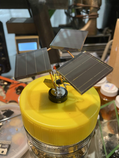 closeup photo of small free-form circuit with a triangular array of three glass square solar panels. it is sitting atop a jar lid