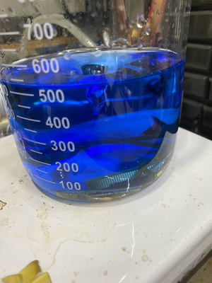 beaker of blue liquid with green and gold rectangles visible in the bottom of the solution